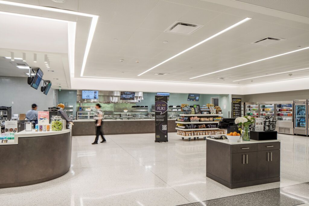 Modern university café and dining area with food service counters, grab-and-go displays, and seating within a bright, open interior.